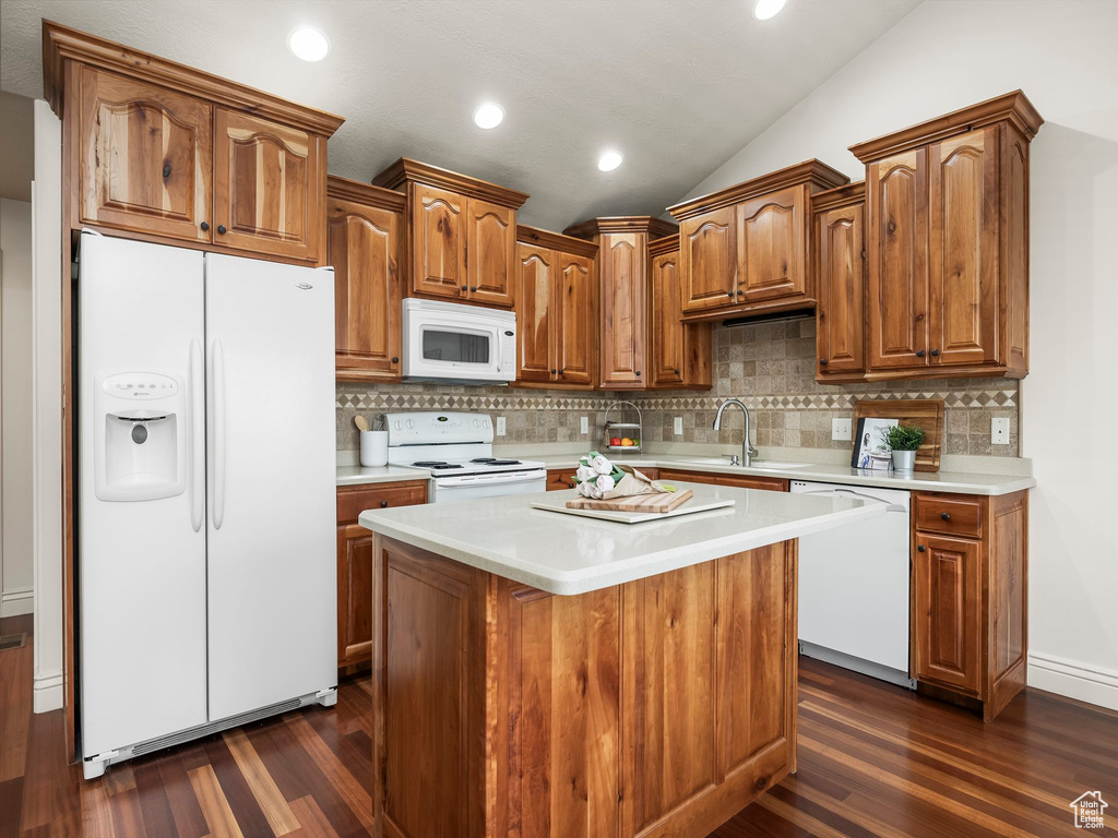 Kitchen featuring white appliances, light countertops, dark wood-type flooring, decorative backsplash, and lofted ceiling