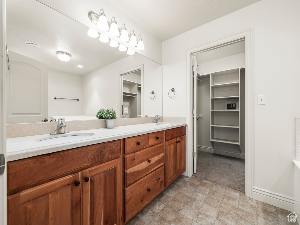 Bathroom with double vanity, a walk in closet, and stone finish flooring
