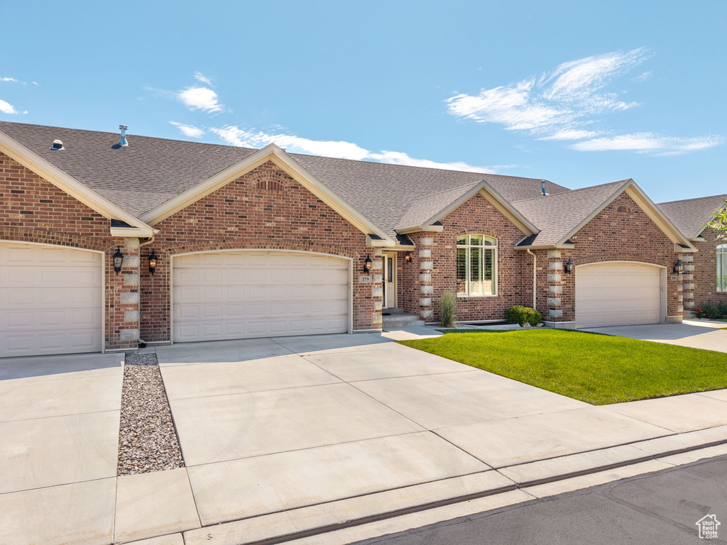 View of front of property with a shingled roof, brick siding, driveway, and a garage