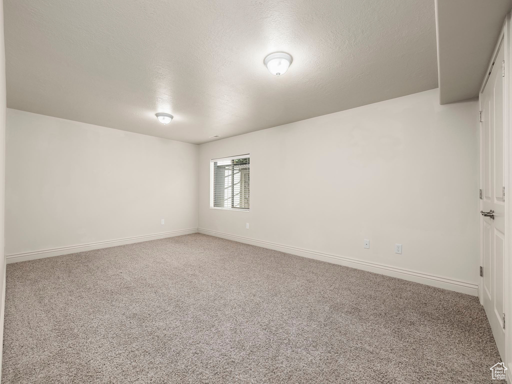 Carpeted spare room featuring a textured ceiling and baseboards