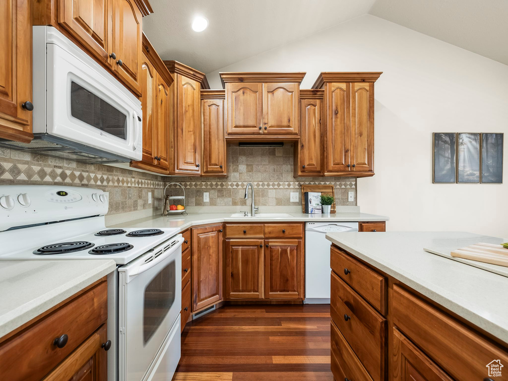 Kitchen featuring white appliances, light countertops, lofted ceiling, dark wood-type flooring, and decorative backsplash