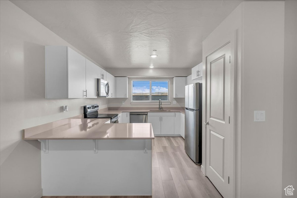 Kitchen with stainless steel appliances, a peninsula, light wood finished floors, white cabinetry, and light countertops