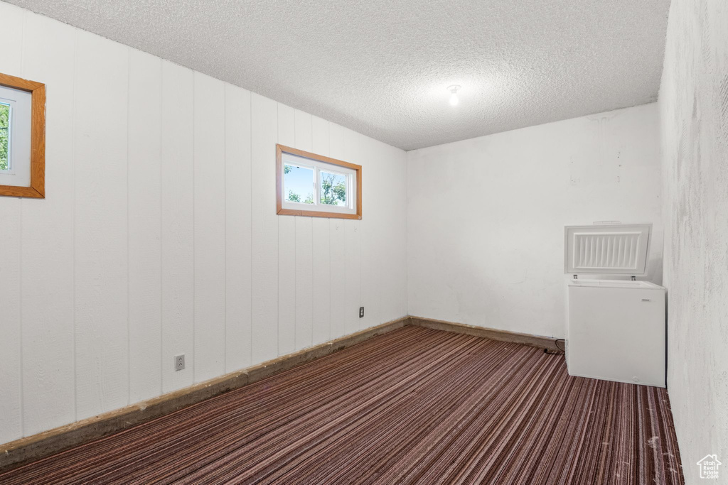 Carpeted empty room with a textured ceiling and baseboards