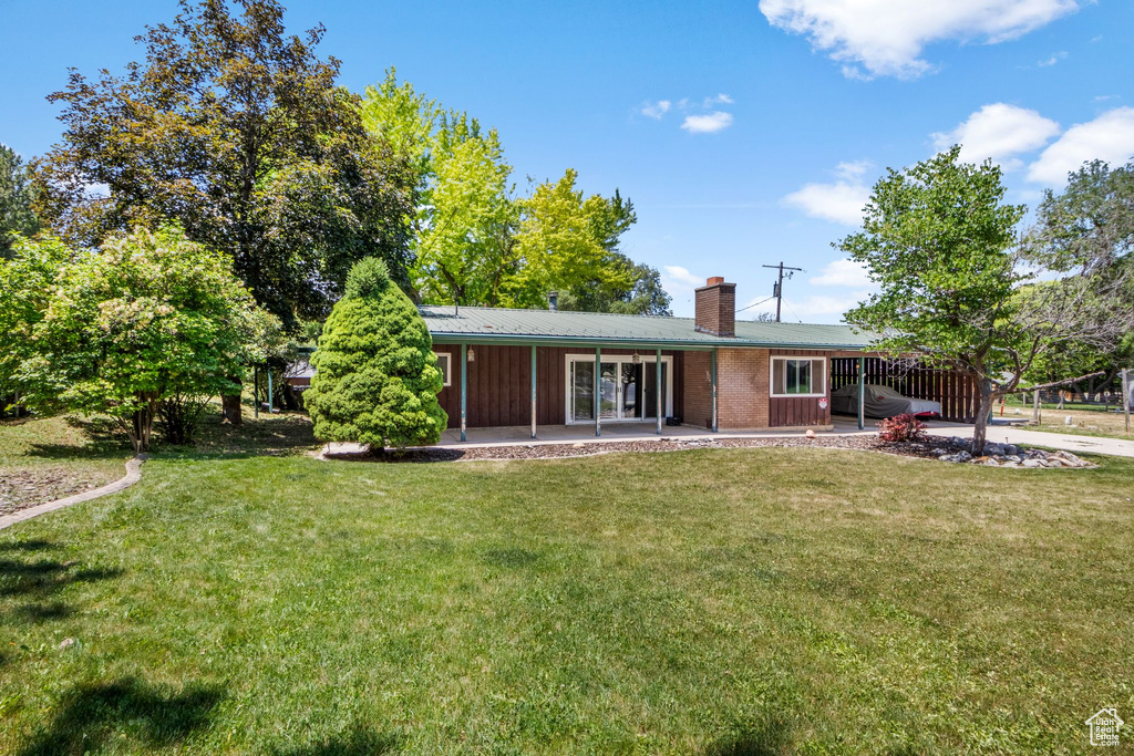 Back of property with a chimney, a lawn, a patio area, and a metal roof