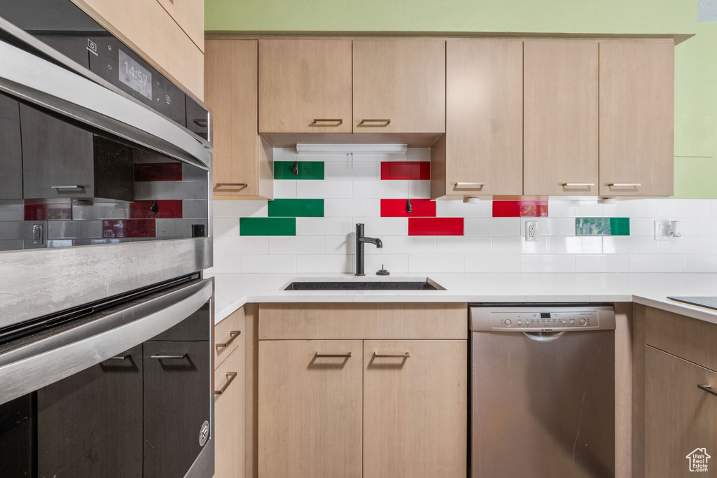 Kitchen with appliances with stainless steel finishes, light brown cabinetry, backsplash, and light countertops