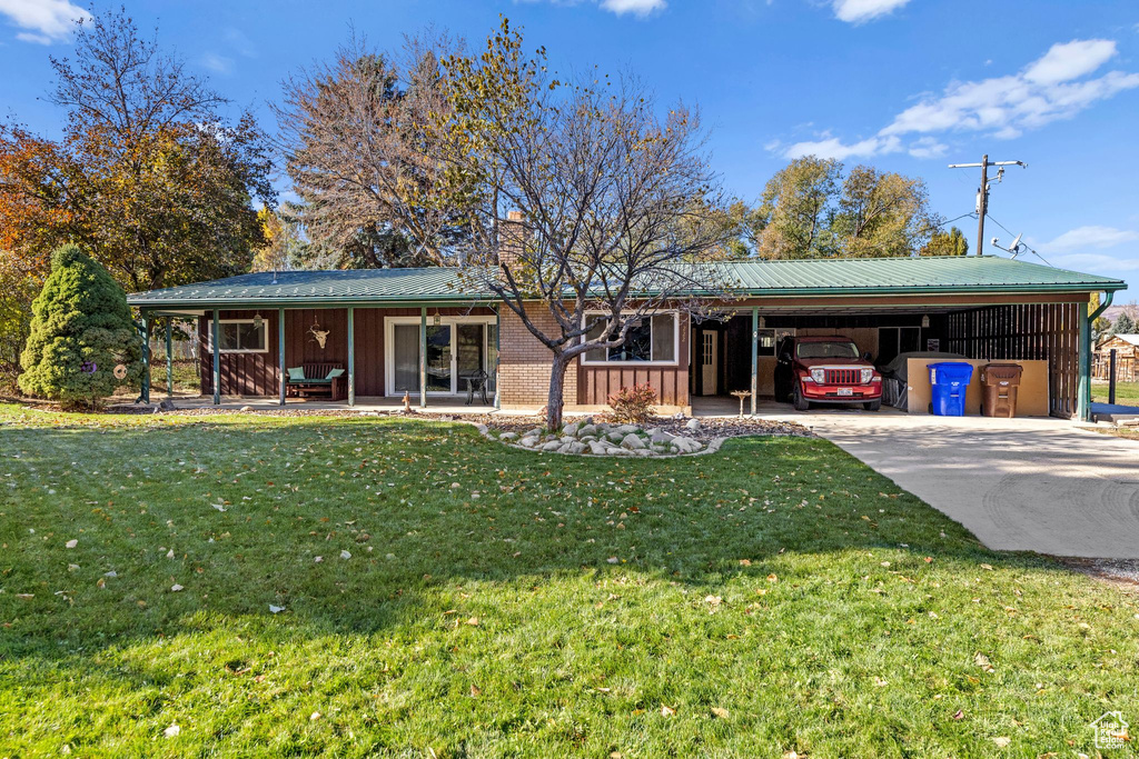 Ranch-style home featuring a chimney, driveway, a front lawn, a carport, and a metal roof