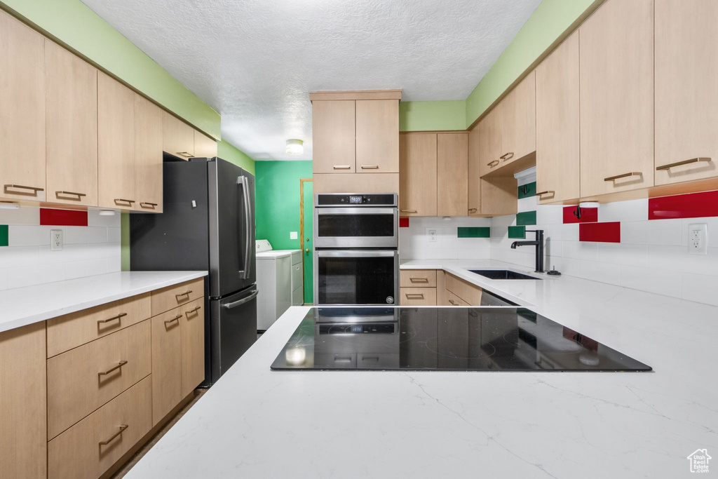 Kitchen featuring light brown cabinetry, washing machine and clothes dryer, appliances with stainless steel finishes, a textured ceiling, and decorative backsplash