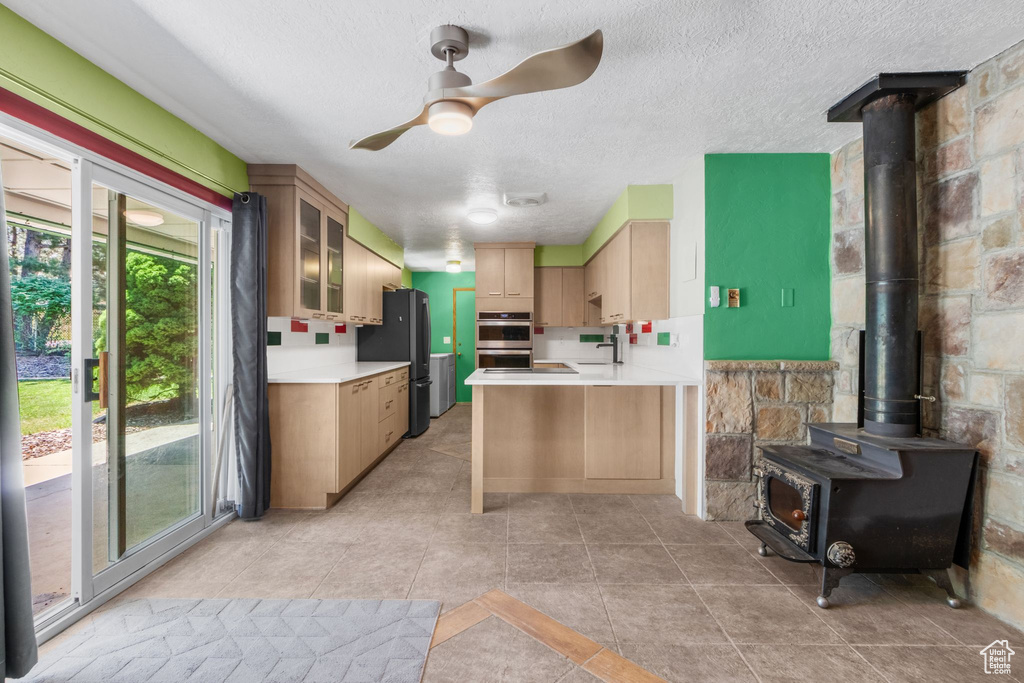 Kitchen with stainless steel appliances, a wood stove, ceiling fan, light countertops, and a textured ceiling