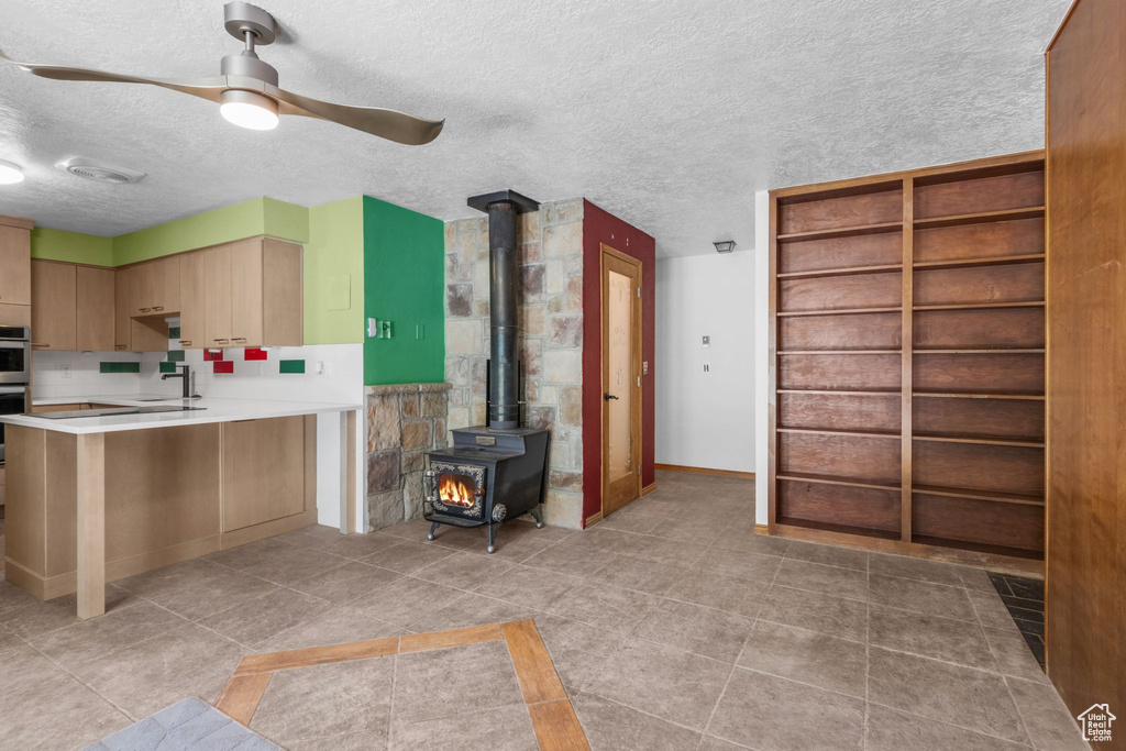 Kitchen featuring a wood stove, a textured ceiling, ceiling fan, light countertops, and a peninsula