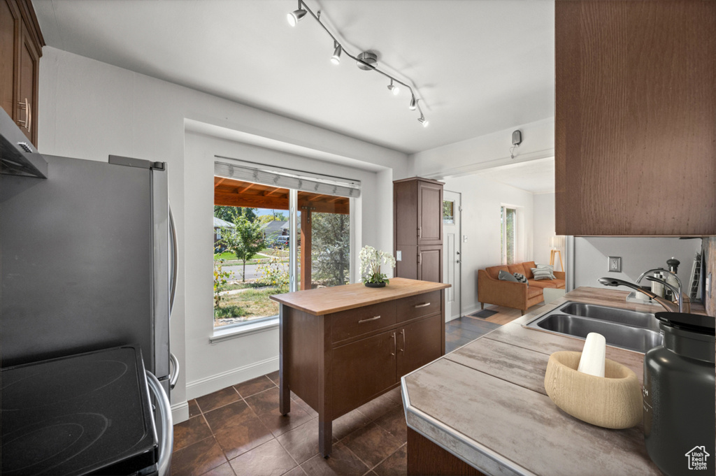 Kitchen with stainless steel appliances, dark tile patterned flooring, dark brown cabinets, and butcher block counters