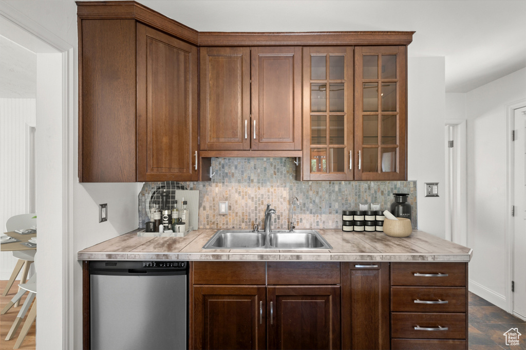 Kitchen featuring stainless steel dishwasher, tasteful backsplash, light countertops, and glass insert cabinets