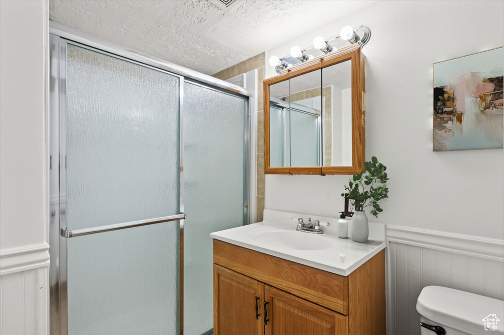 Full bathroom with vanity, a stall shower, a wainscoted wall, a textured ceiling, and a decorative wall