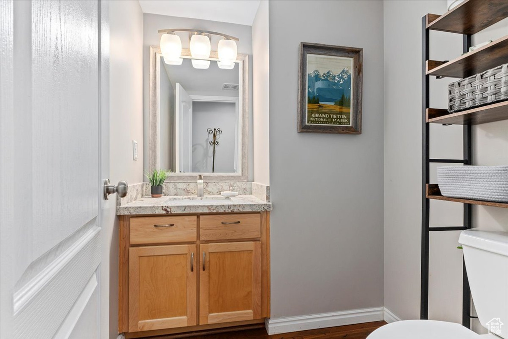 Half bath featuring toilet, vanity, wood finished floors, and baseboards