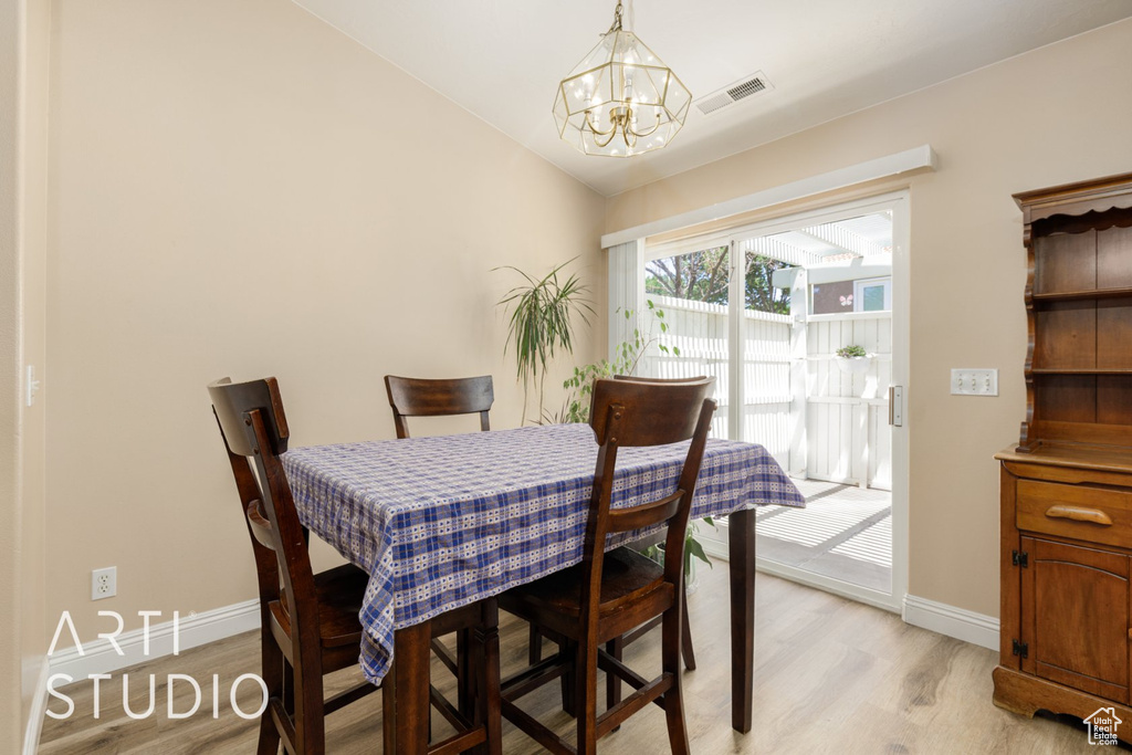 Dining space with a chandelier, light wood-type flooring, baseboards, and vaulted ceiling
