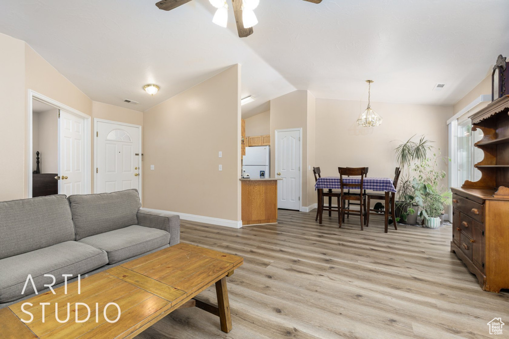 Living room with light wood-style flooring, lofted ceiling, a ceiling fan, a chandelier, and baseboards