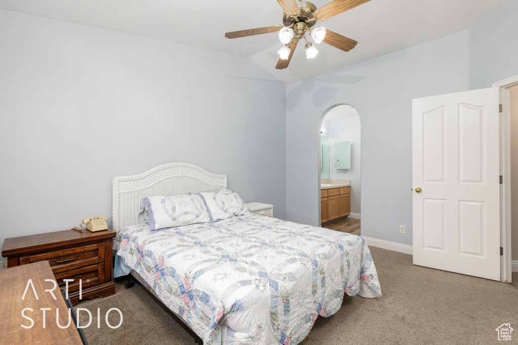 Bedroom featuring light colored carpet, arched walkways, lofted ceiling, baseboards, and connected bathroom