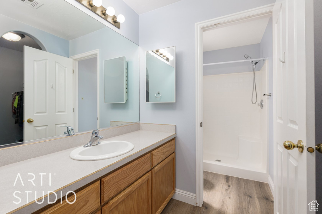 Bathroom featuring wood finished floors, a shower, vanity, and baseboards