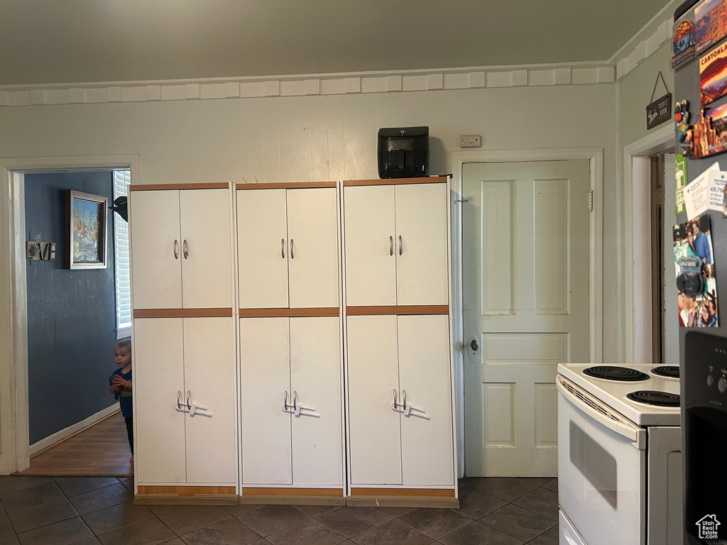 Kitchen featuring white range with electric stovetop, dark tile patterned floors, and white cabinets