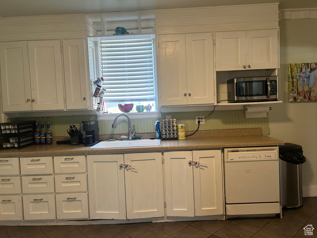 Kitchen featuring dishwasher, stainless steel microwave, white cabinetry, and dark tile patterned flooring