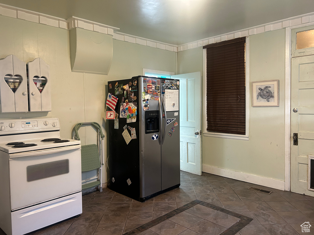 Kitchen with white electric range oven, stainless steel fridge, and dark tile patterned flooring