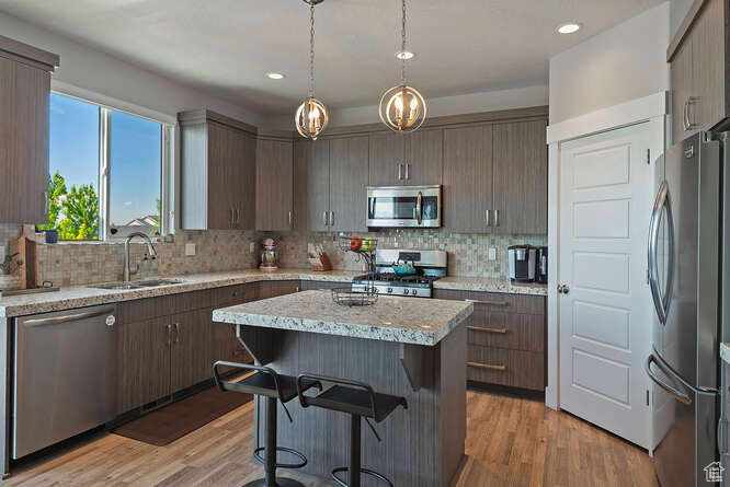 Kitchen featuring appliances with stainless steel finishes, a kitchen island, backsplash, a kitchen bar, and light wood-style floors