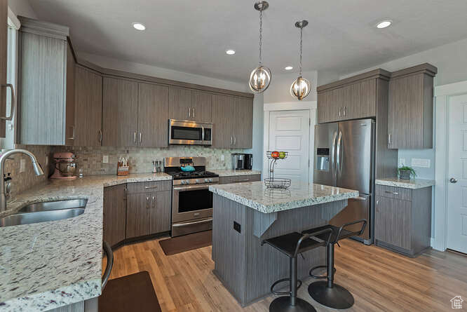 Kitchen with appliances with stainless steel finishes, a center island, tasteful backsplash, light wood-style floors, and light stone countertops