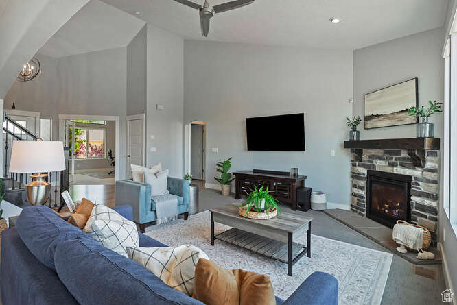 Living room with high vaulted ceiling, a stone fireplace, stairway, a ceiling fan, and arched walkways