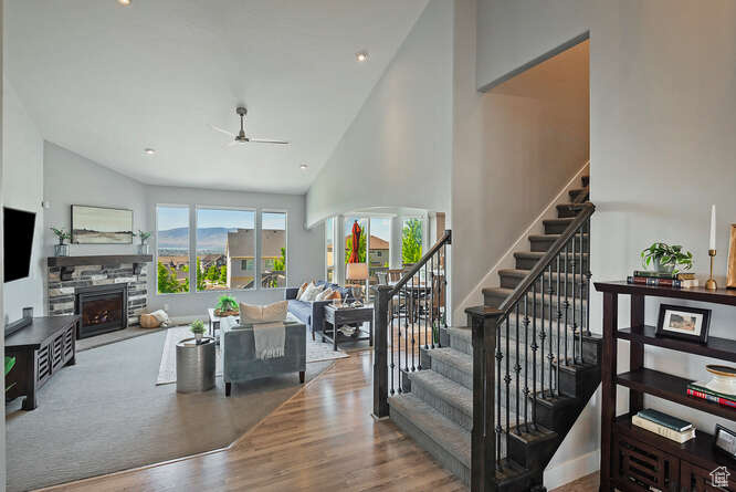 Stairs featuring ceiling fan, high vaulted ceiling, a fireplace, and wood finished floors