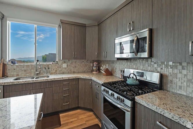 Kitchen featuring stainless steel appliances, backsplash, light wood-type flooring, and light stone countertops