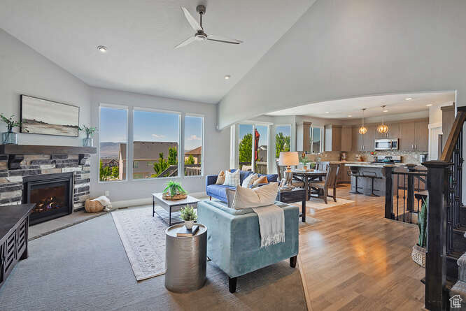 Living area featuring a ceiling fan, a stone fireplace, high vaulted ceiling, light wood-type flooring, and recessed lighting