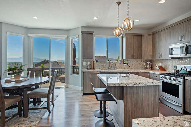 Kitchen featuring stainless steel appliances, recessed lighting, tasteful backsplash, an island with sink, and light wood-style flooring