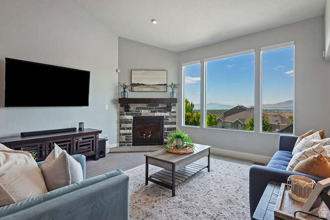 Carpeted living room with a stone fireplace and vaulted ceiling