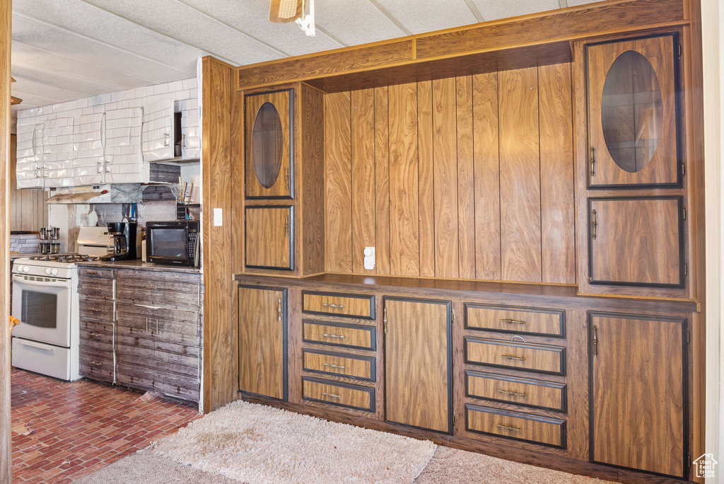 Kitchen with white range with gas stovetop, brick patterned flooring, brown cabinets, and wood walls
