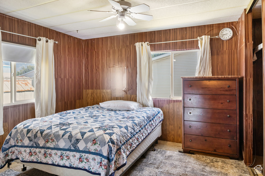 Bedroom with carpet floors, wooden walls, and a ceiling fan