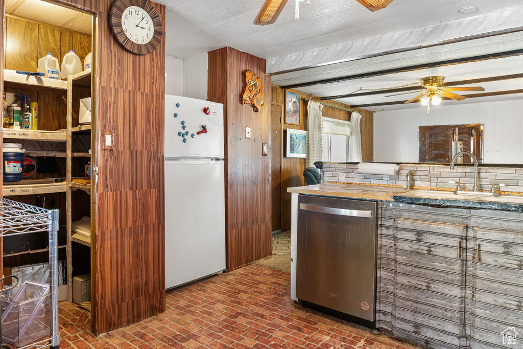 Kitchen featuring stainless steel dishwasher, ceiling fan, a sink, freestanding refrigerator, and wooden walls