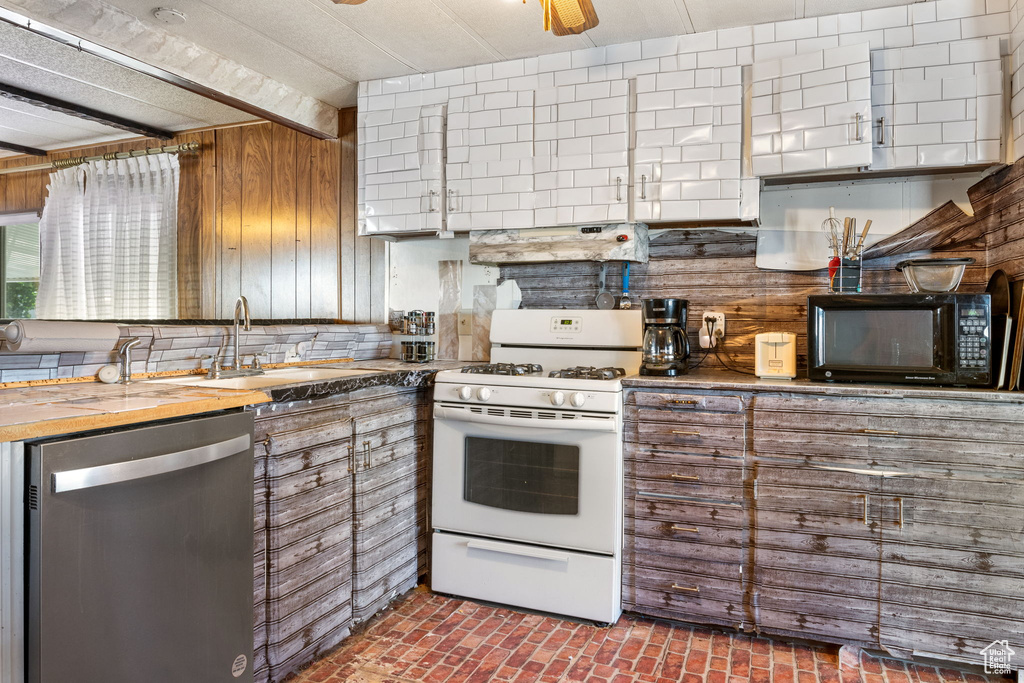 Kitchen featuring dishwasher, black microwave, white gas range oven, brick patterned flooring, and a sink