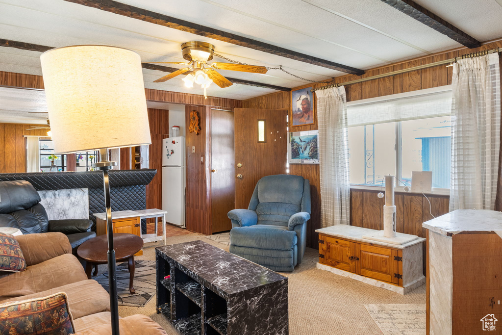 Living area featuring wooden walls, ceiling fan, beamed ceiling, and light carpet