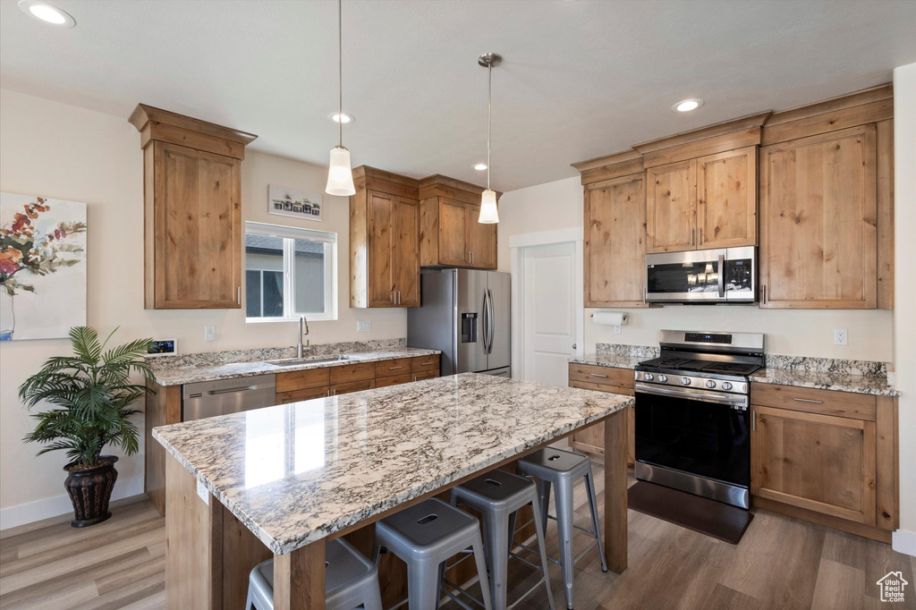 Kitchen featuring stainless steel appliances, light wood-type flooring, a breakfast bar, light stone counters, and recessed lighting