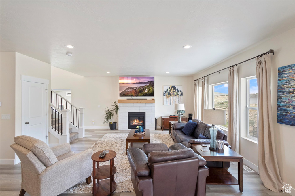Living room with light wood-style floors, a tiled fireplace, recessed lighting, and stairway