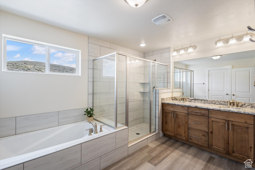 Bathroom with a shower stall, a bath, double vanity, and wood finished floors