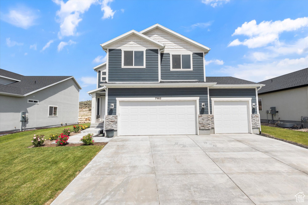 View of front of property featuring a front lawn, driveway, stone siding, and an attached garage