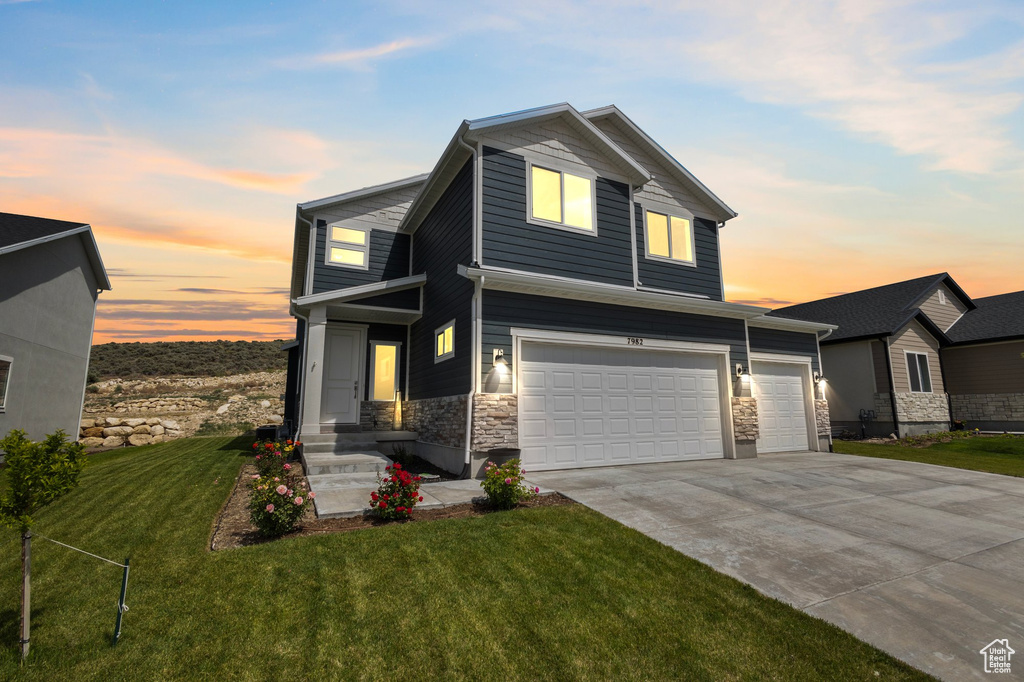 View of front of house featuring stone siding, a lawn, driveway, and an attached garage