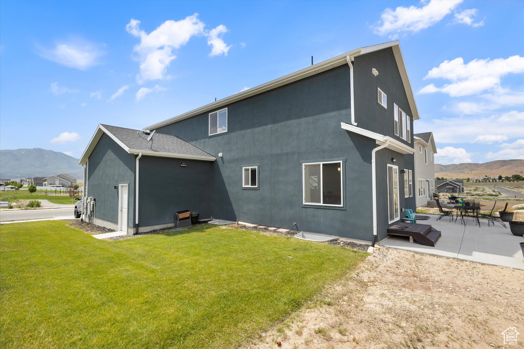 Back of house with a mountain view, stucco siding, a patio area, and a yard