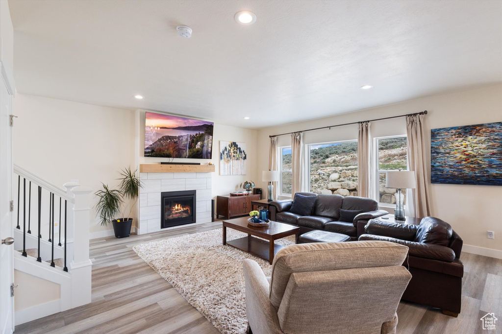 Living room with light wood-style floors, a tiled fireplace, recessed lighting, and stairway