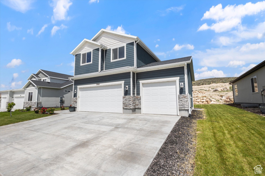 View of front facade featuring stone siding, a front lawn, concrete driveway, and an attached garage