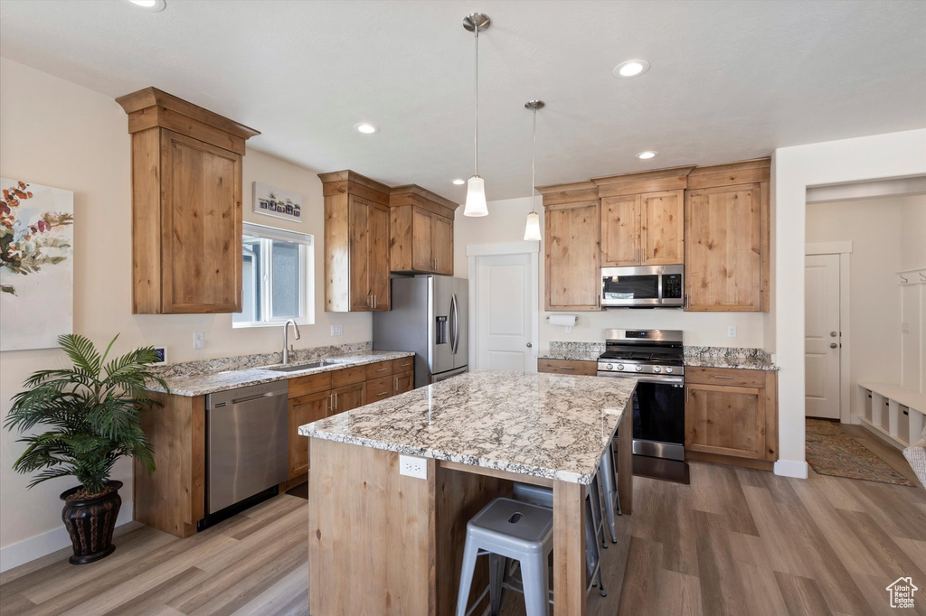 Kitchen featuring appliances with stainless steel finishes, light wood-style flooring, a kitchen island, light stone countertops, and recessed lighting