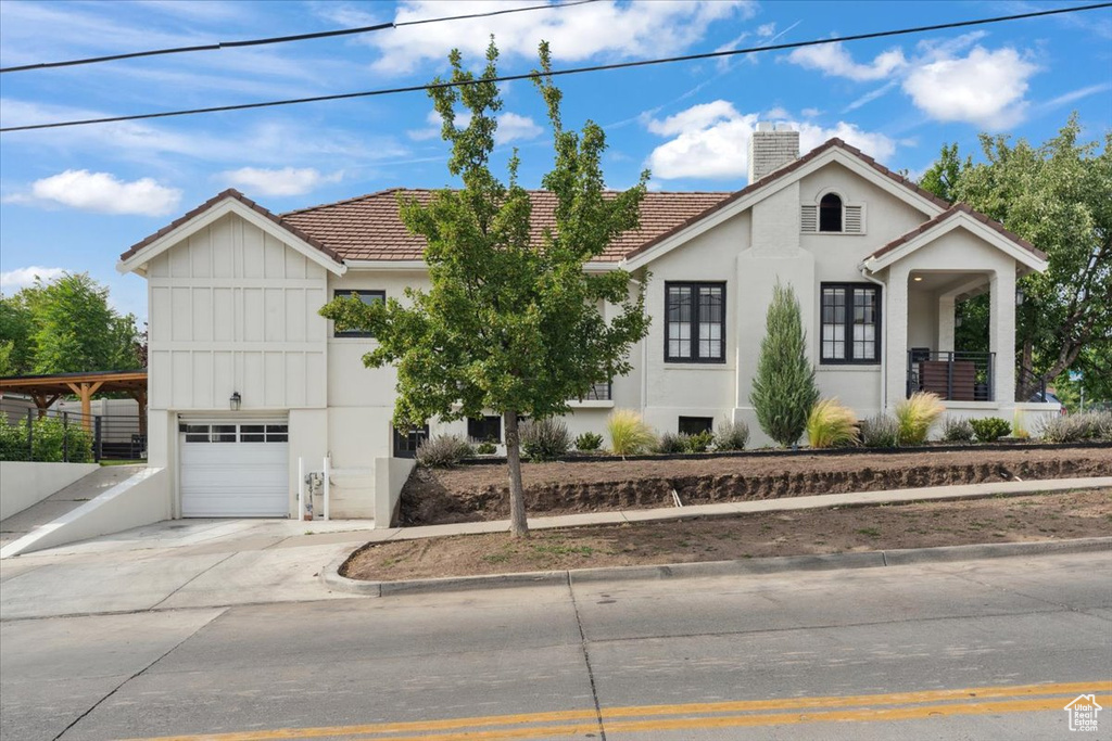 View of front of house with a chimney, a tile roof, a garage, and stucco siding