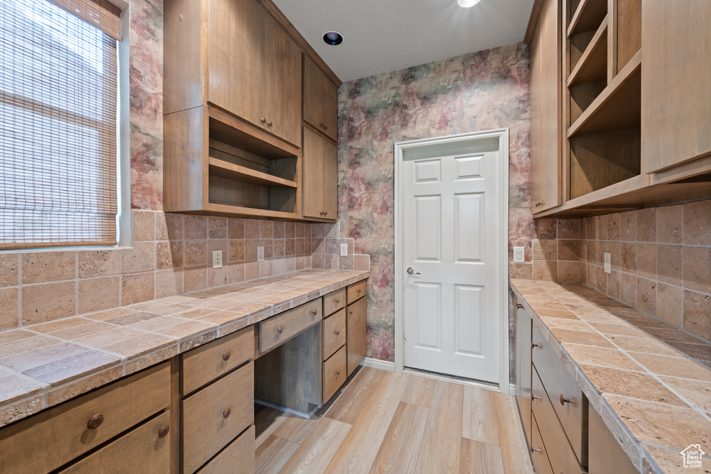 Kitchen with open shelves, tile counters, tasteful backsplash, and light wood finished floors
