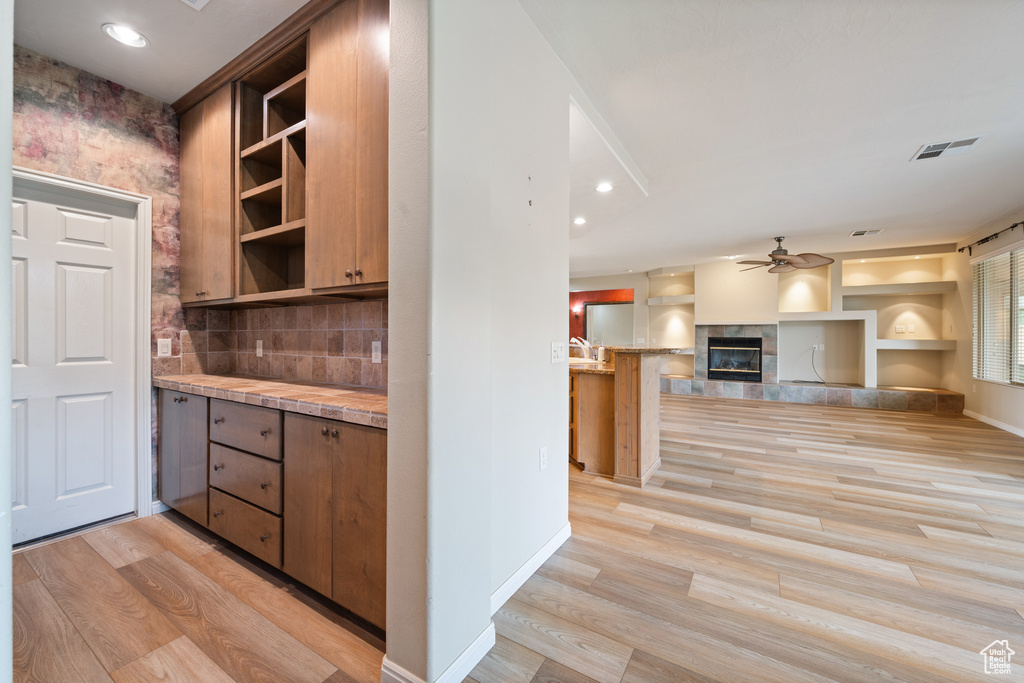 Kitchen with light wood-style floors, a ceiling fan, open shelves, light countertops, and a tile fireplace