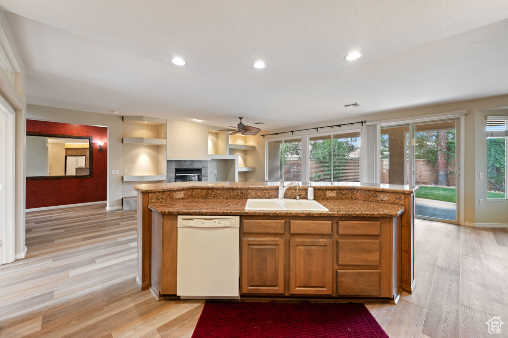 Kitchen with dishwasher, a fireplace, a ceiling fan, light wood-style flooring, and an island with sink